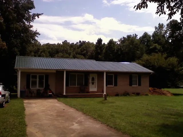 Dark green metal roof on a brick ranch with a covered porch in Bellwood